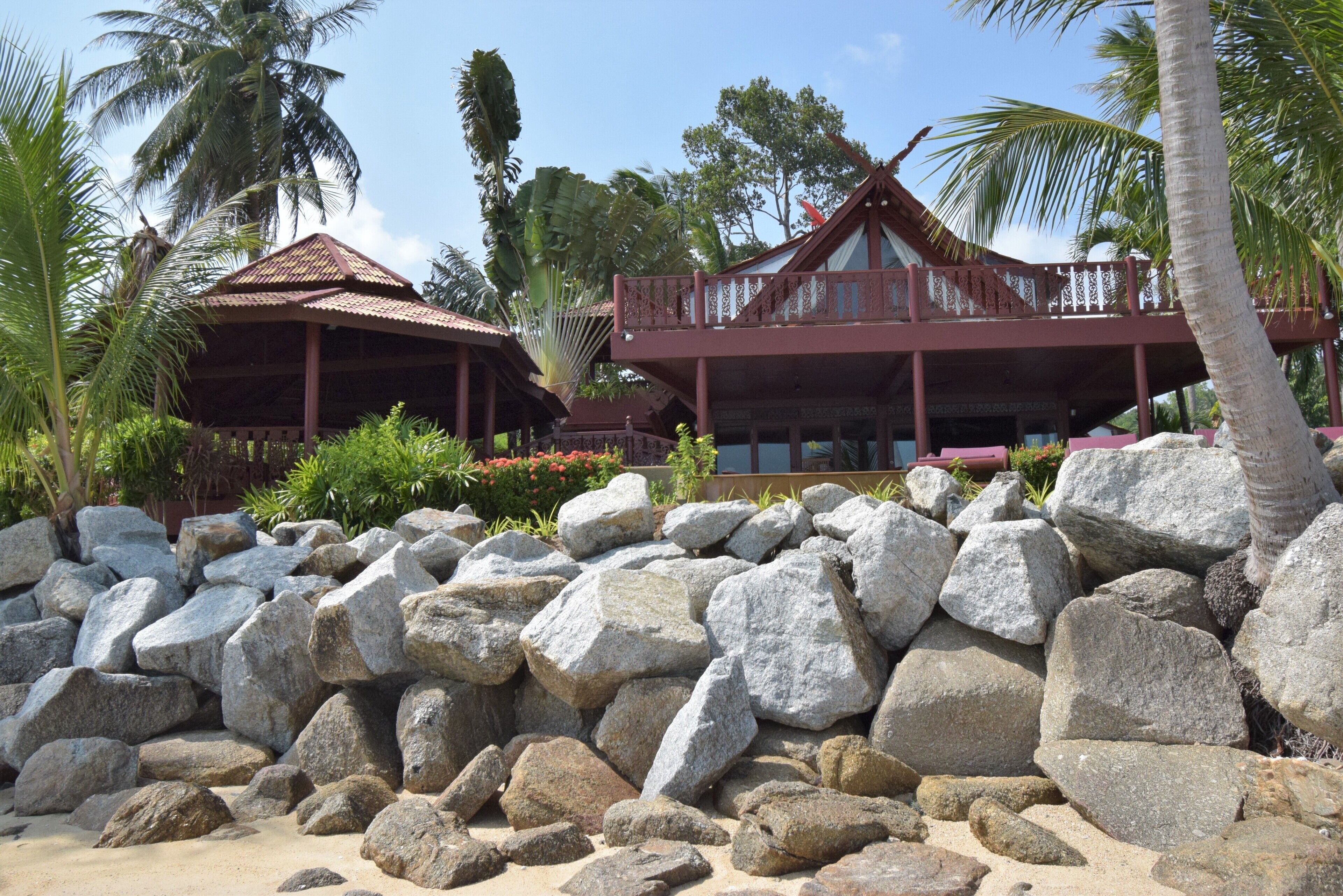 A resort with a large rock garden, a wooden structure with a thatched roof, and a balcony overlooking the garden.
