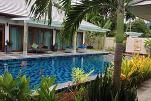 A poolside area with a tiled pool, lounge chairs, and tropical plants.