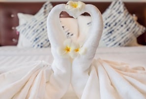 Una toalla doblada con forma de corazón y flores sobre una cama con almohadones a rayas.