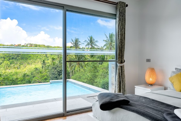 A bedroom with a large window overlooking a swimming pool and lush greenery. - 3 Bedroom Sea View Villa Mikia SDV007 - By Samui Dream Villas (Koh Samui)