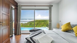 A bedroom with a large window, a bed, a nightstand, and a view of a swimming pool and greenery. - 3 Bedroom Sea View Villa Mikia SDV007 - By Samui Dream Villas (Koh Samui)
