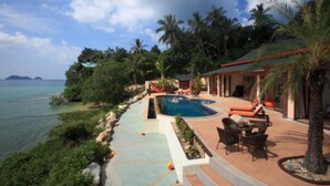 A pool area with a view of the sea, surrounded by palm trees and a building with a red roof. - 8 Bedroom Sea Front Twin Villa Koh Phangan SDV231/234-By Samui Dream Villas  (Ko Pha-ngan)