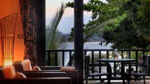 A balcony with wicker furniture and a table with glasses, overlooking a body of water and greenery. - 8 Bedroom Sea Front Twin Villa Koh Phangan SDV231/234-By Samui Dream Villas  (Ko Pha-ngan)