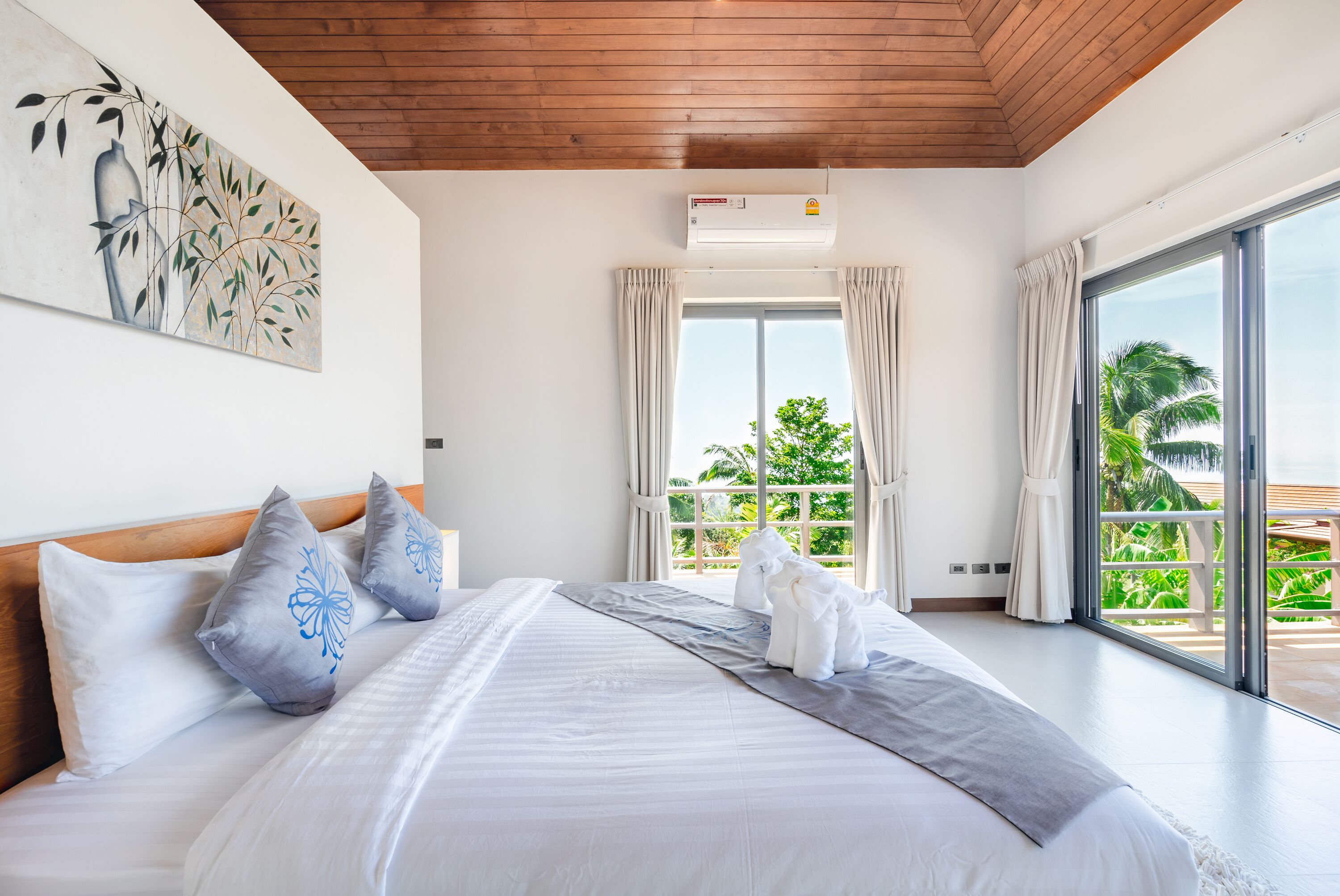 Habitación de hotel con una cama grande, un ventilador de techo, una ventana con cortinas y vistas a palmeras.