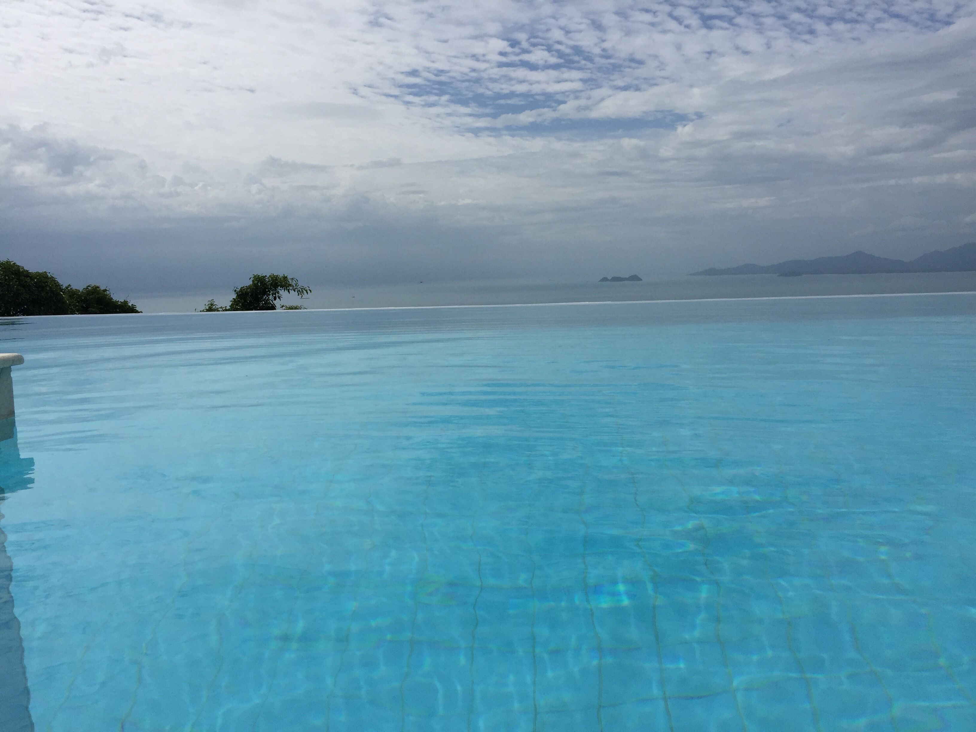 A clear blue infinity pool with a view of the ocean and distant islands.