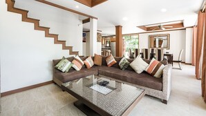 A modern living room with a brown sectional sofa, a glass coffee table, and a wooden staircase. - 7 Bedroom Twin Villas TG48+TG25 on Beach Front Resort SDV282/288-By Samui Dream Villas (Koh Samui)