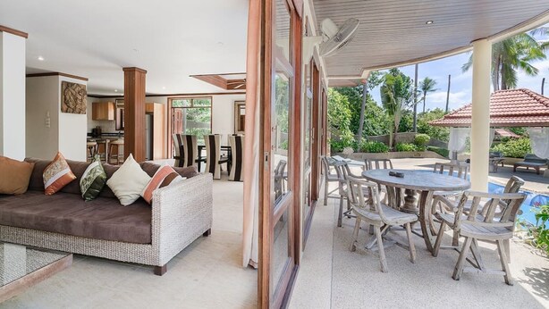 A modern living area with a sofa, dining table, and chairs. There is a large window providing a view of the outdoors. - 7 Bedroom Twin Villas TG48+TG25 on Beach Front Resort SDV282/288-By Samui Dream Villas (Koh Samui)