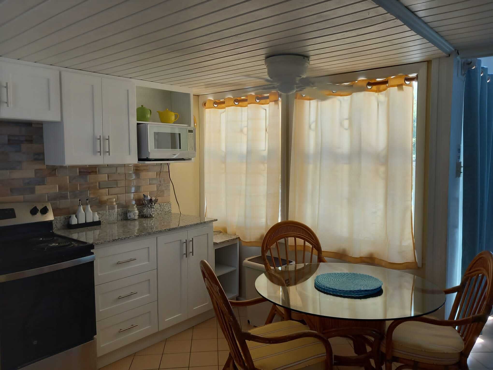 A kitchen with white cabinets, a microwave, and a stove. There is a dining table with chairs and a blue placemat.