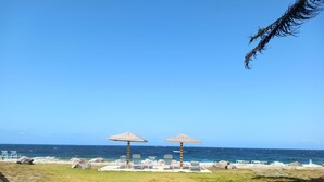 Una playa con dos sombrillas de madera y sillas de descanso.