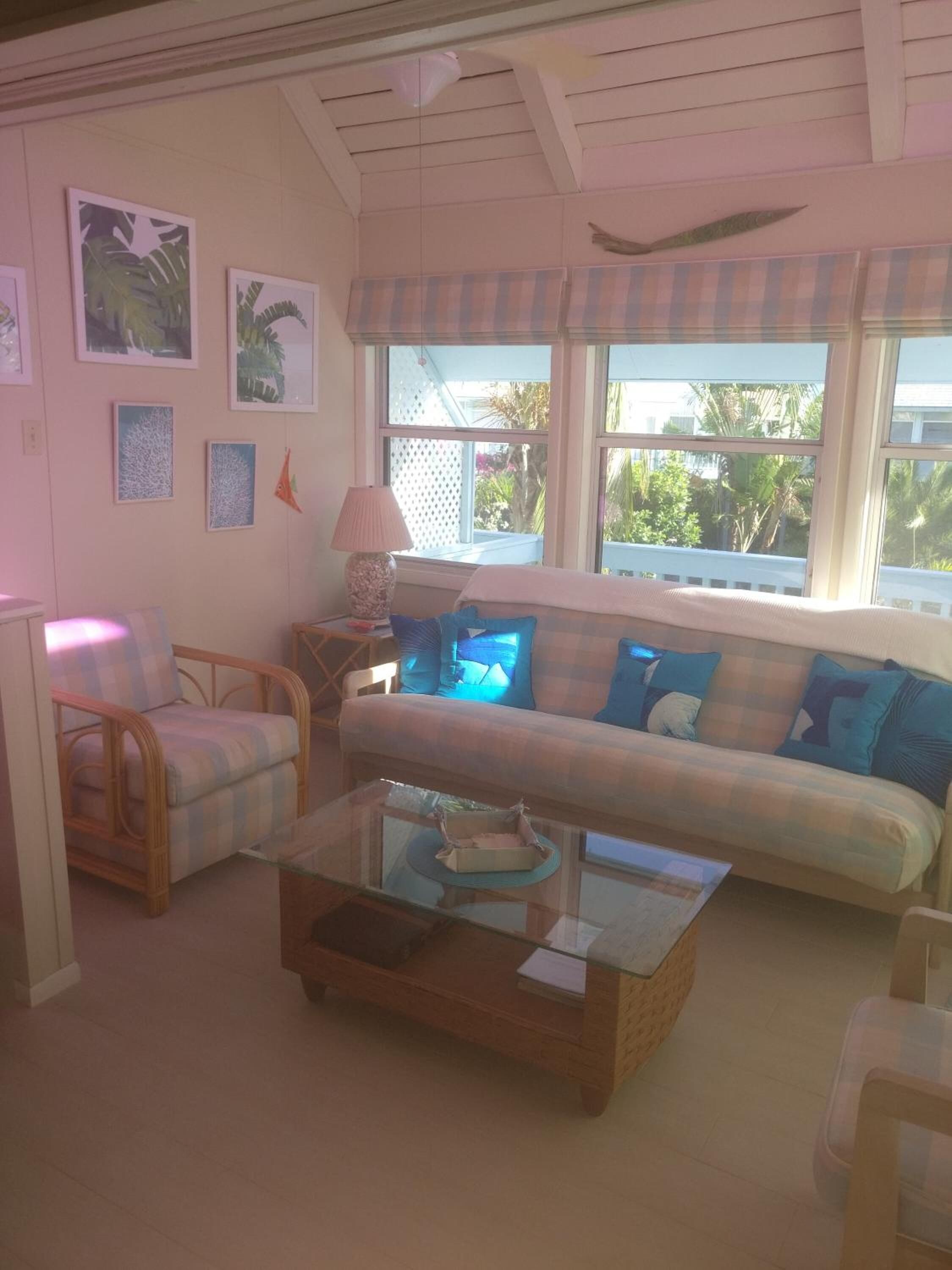 Una sala de estar con un sofá, sillones, una mesita de centro y una lámpara. Se ven ventanas con vistas a espacios verdes.