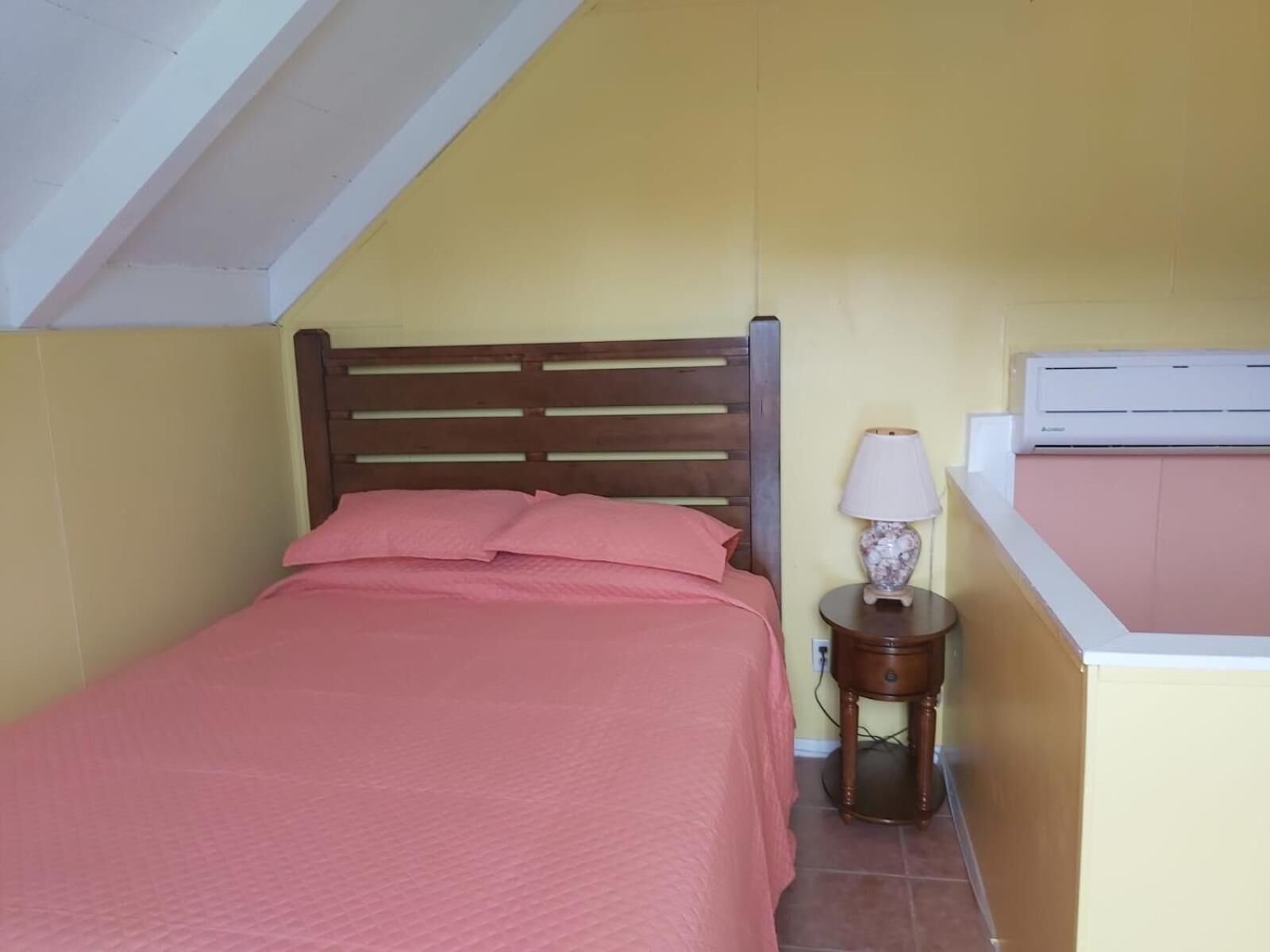 A bedroom with a bed, a bedside table with a lamp, and an air conditioning unit.