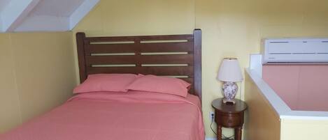 A bedroom with a bed, a bedside table with a lamp, and an air conditioning unit.