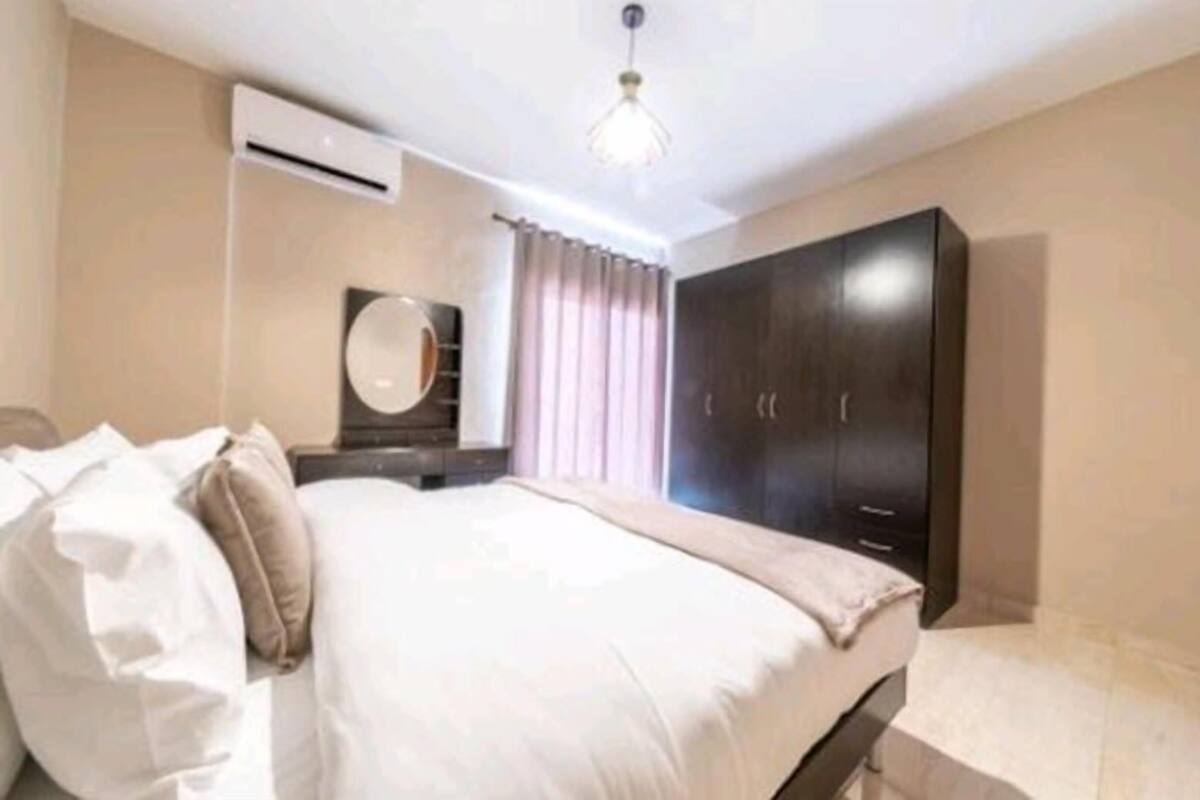 A bedroom with a bed, a wardrobe, a mirror, and an air conditioning unit.