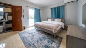 Ein Schlafzimmer mit Bett, ein Badezimmer mit Waschbecken und ein großes Fenster mit Vorhängen.