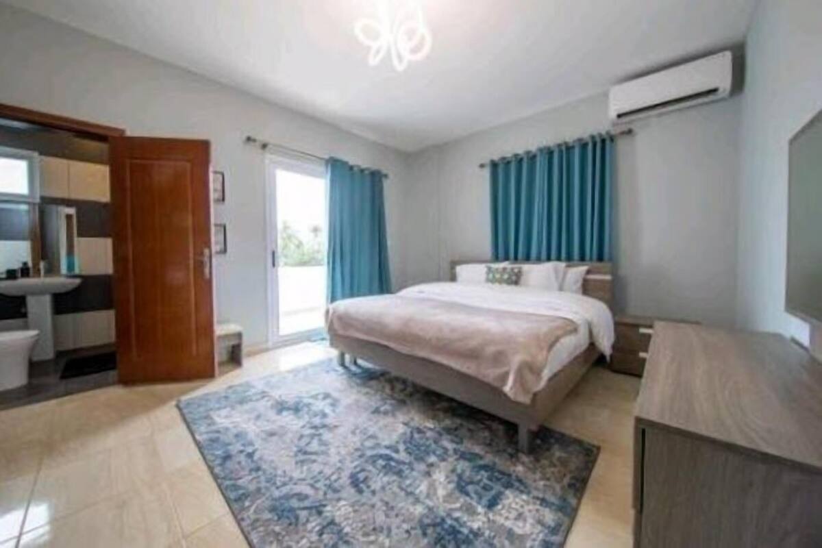 A bedroom with a bed, a bathroom with a sink, and a large window with curtains.