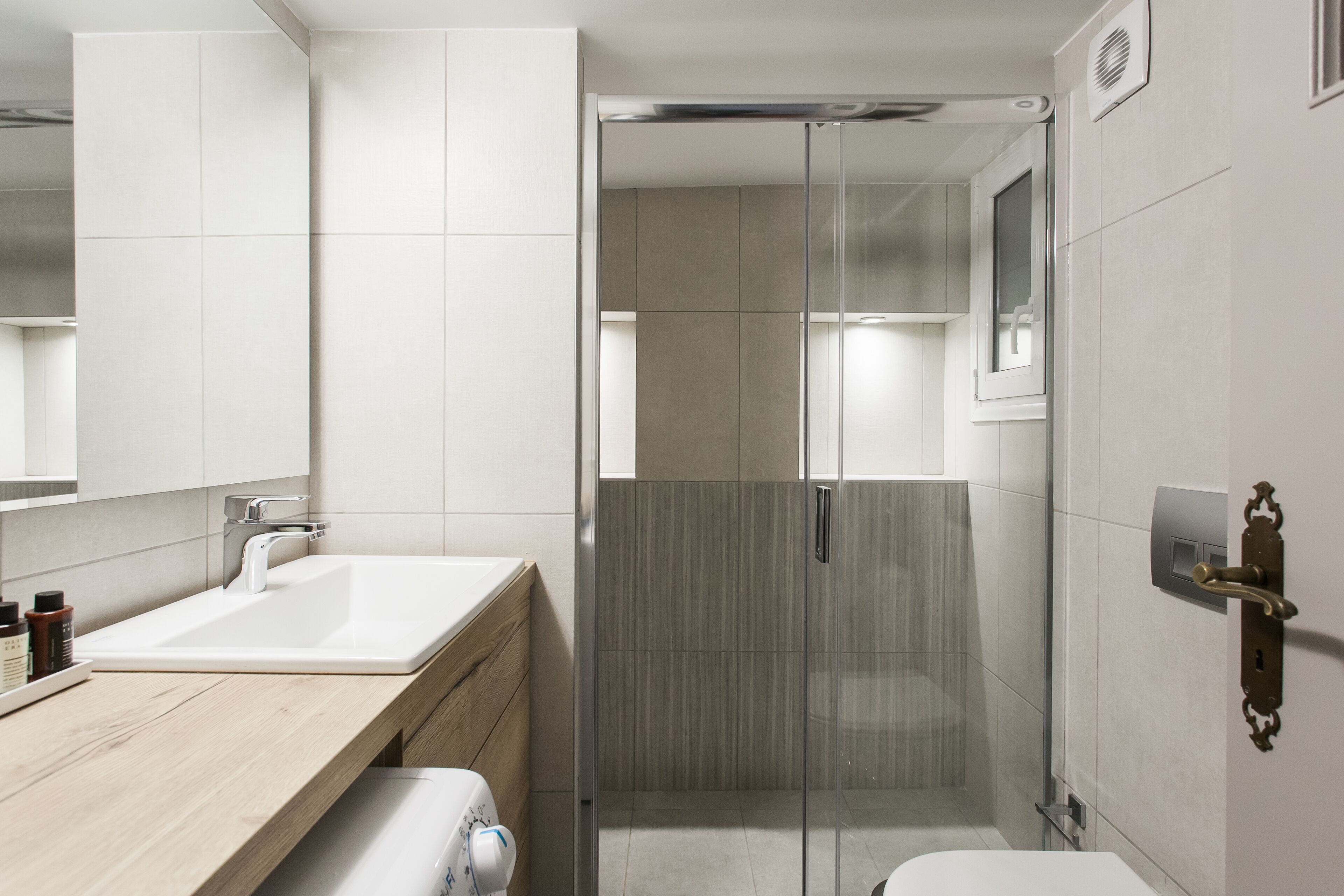 A modern bathroom with a white sink, wooden vanity, glass shower enclosure, and a toilet.