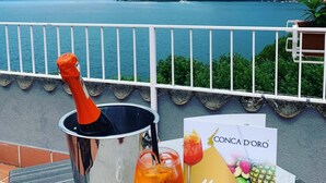 Une terrasse avec vue sur un lac et des montagnes, une bouteille de champagne, un verre de vin rouge et une enseigne indiquant le menu.