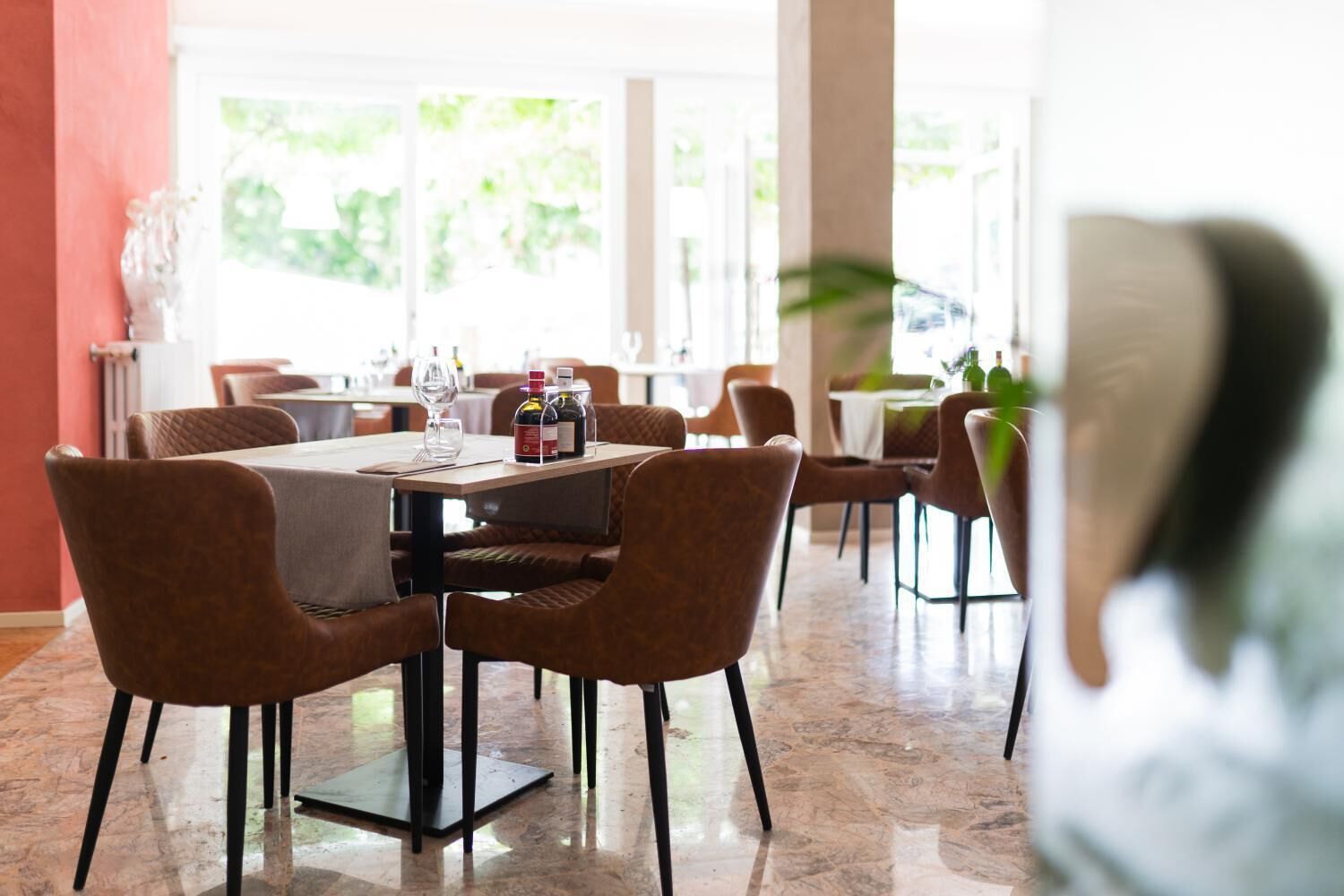 Un comedor con mesas y sillas, piso de mármol y vistas al exterior.