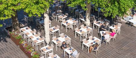 Een terras met meerdere tafels en stoelen, omringd door bomen.