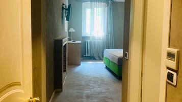 Un couloir menant à une chambre à coucher équipée d’un lit, d’un radiateur et d’une fenêtre avec des rideaux.