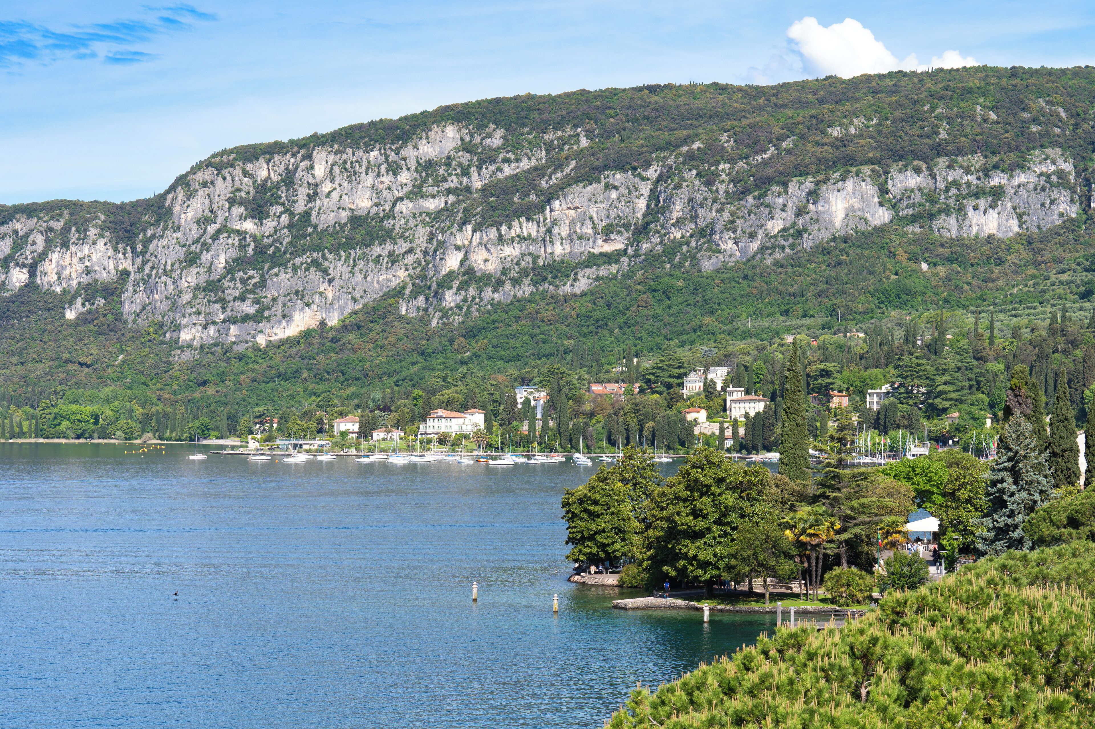 Un lac avec des bateaux, une colline boisée et des bâtiments en arrière-plan.