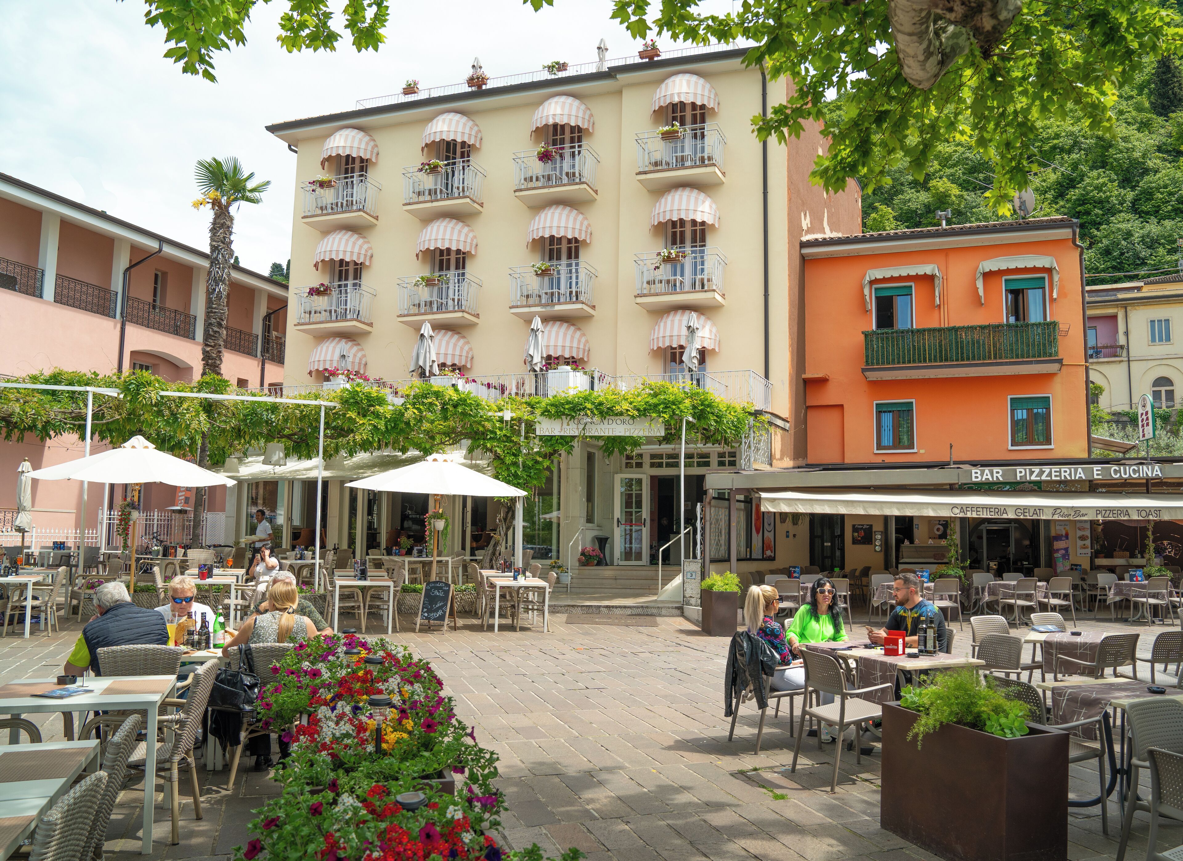 An outdoor cafe area with tables and chairs, surrounded by buildings with balconies and awnings.