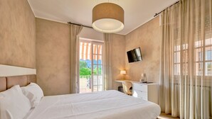 Une chambre d’hôtel avec un grand lit, un bureau avec une chaise, un téléviseur fixé au mur et un balcon avec des rideaux.