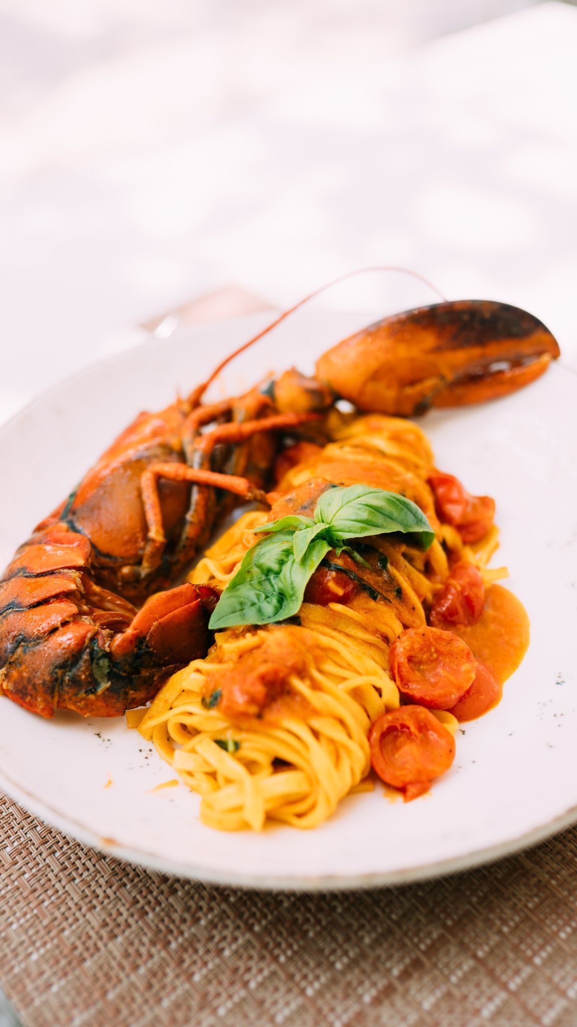 A plate with pasta, a lobster, and a basil leaf.