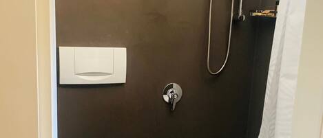 A small, dark-colored bathroom with a white toilet, a shower with a handheld showerhead, and a towel rack.