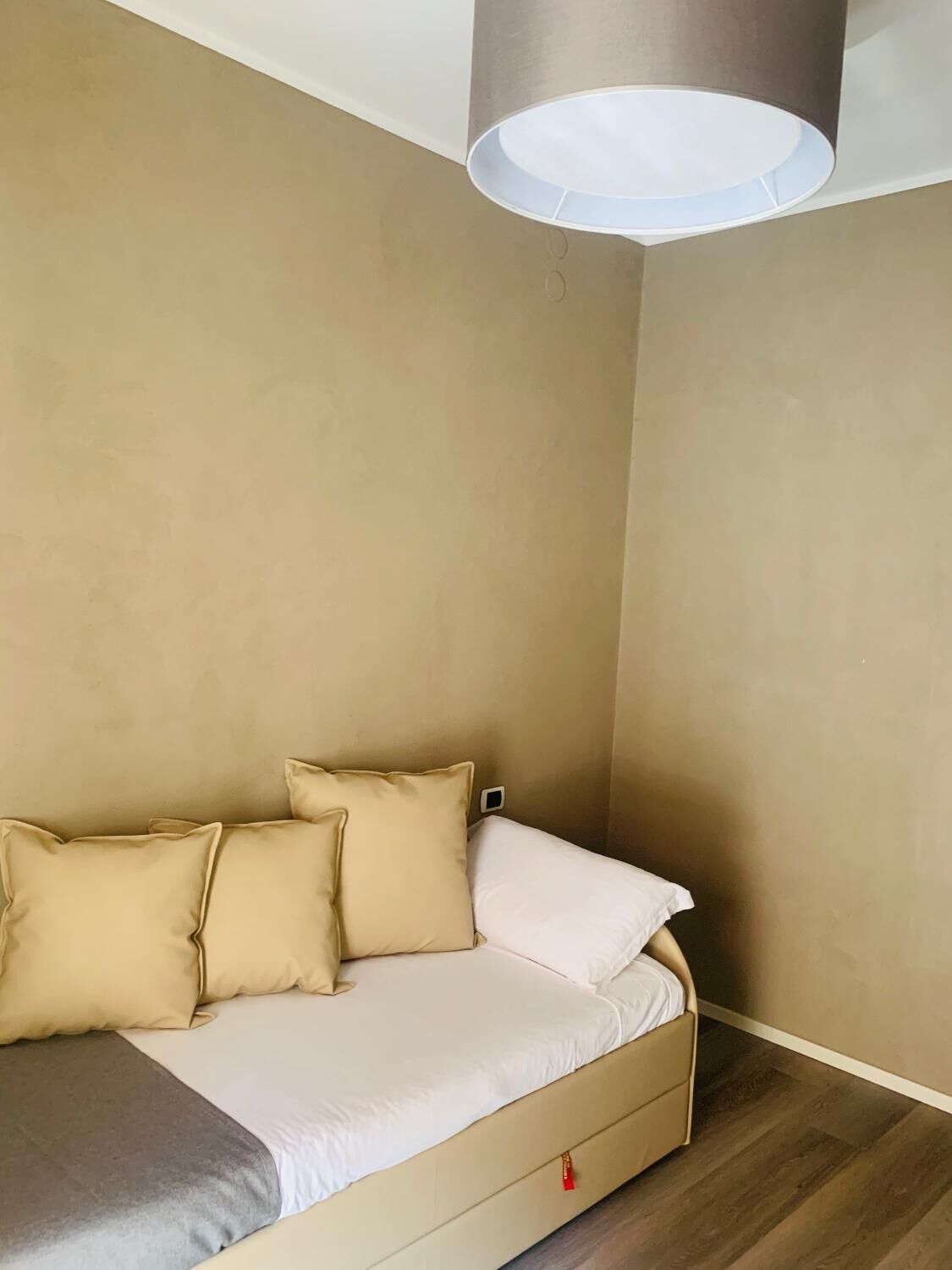 Un dormitorio con cama, paredes color beige y lámpara en el techo.
