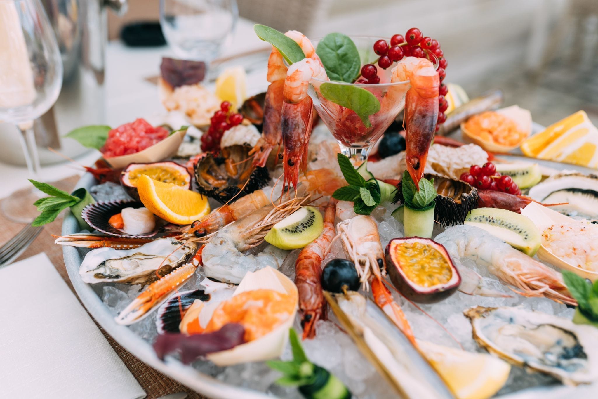 Una bandeja de mariscos con camarones, ostras y diversas frutas sobre hielo.