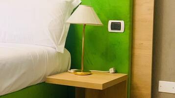 Una cama con cabecera verde, una mesita de noche con lámpara y un enchufe en la pared.