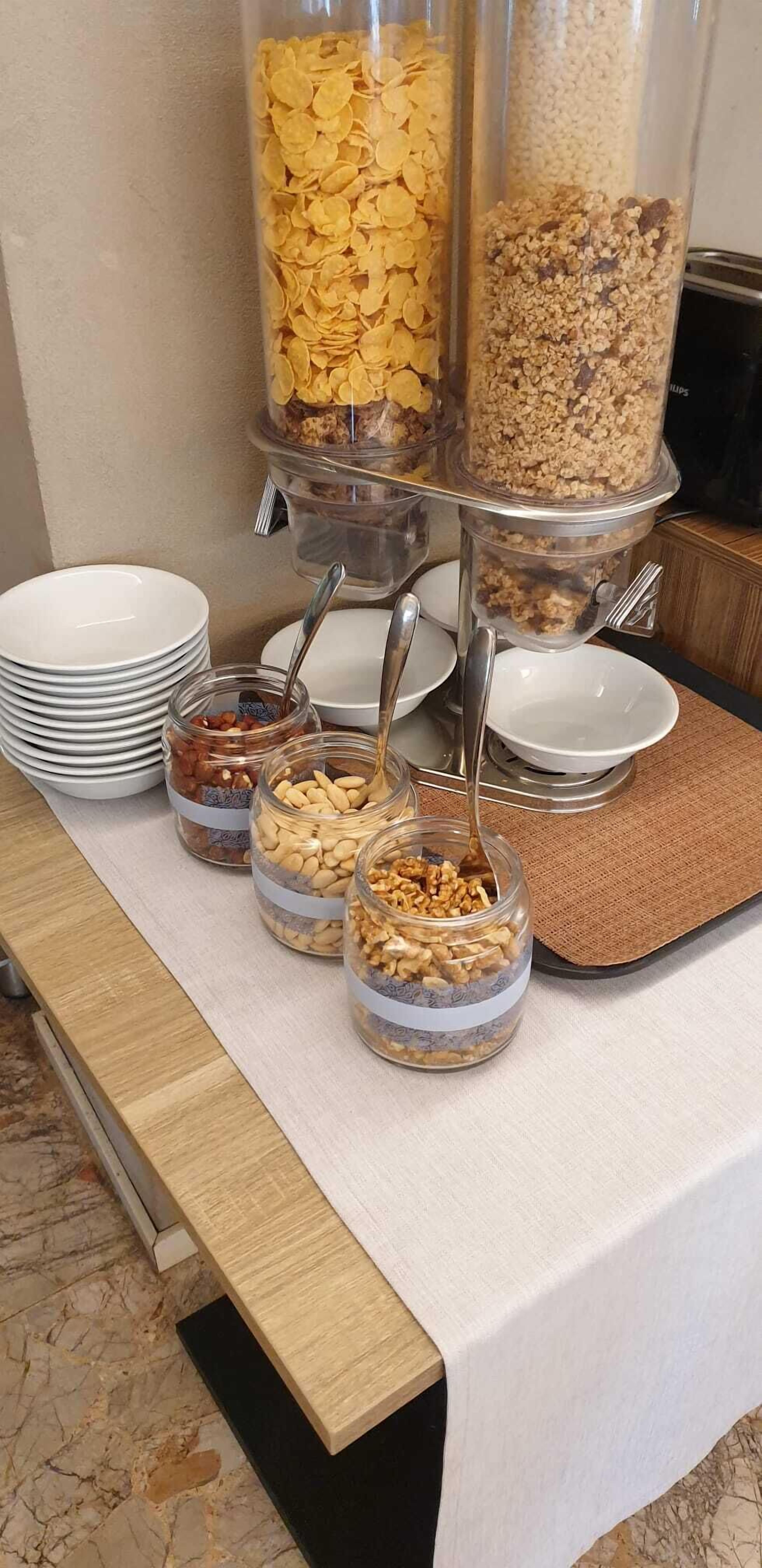 Un buffet con diversi cibi esposti in contenitori, tra cui cereali, granola e frutta secca.