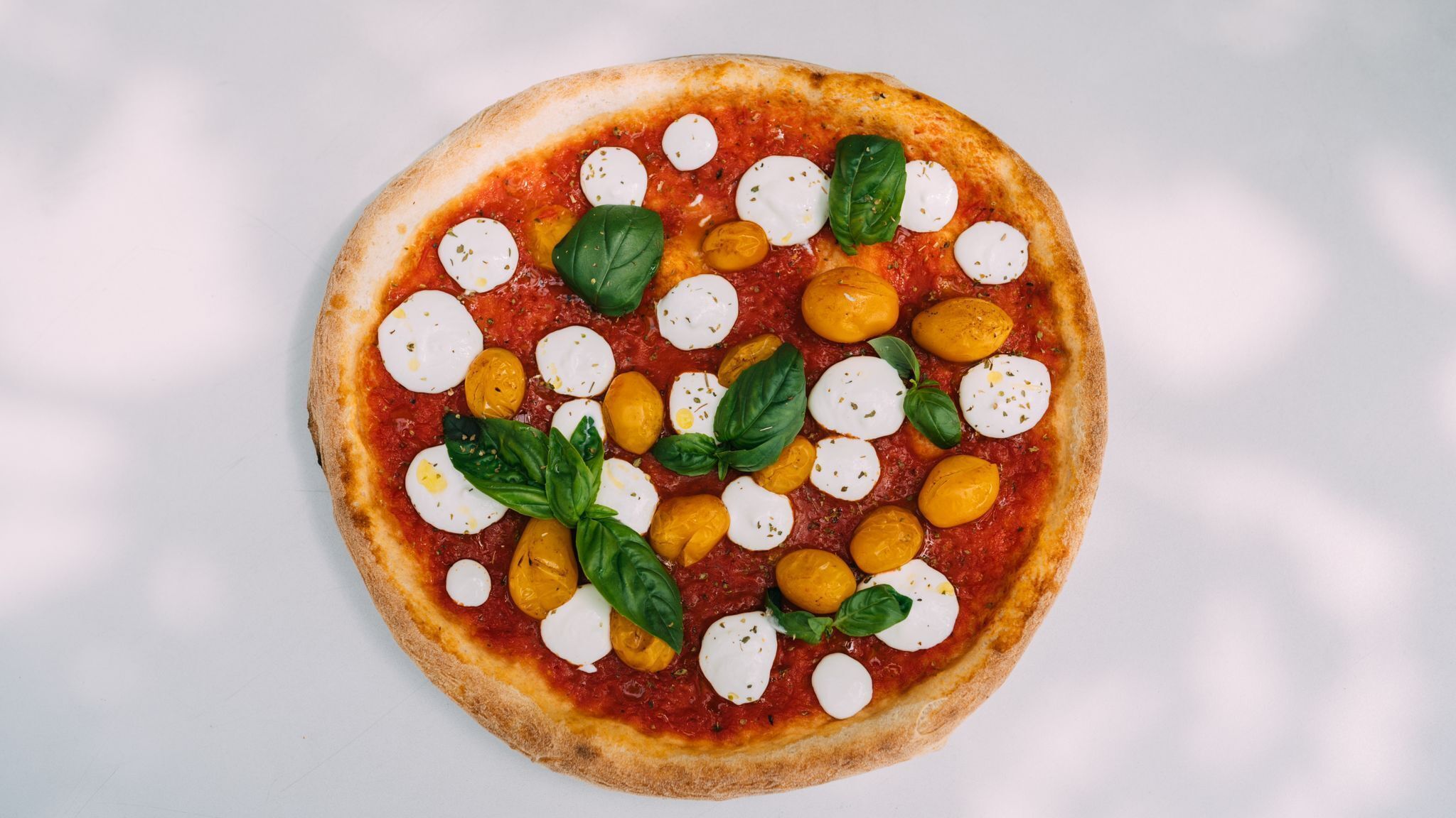 Pizza con mozzarella, basilico e pomodorini ciliegino su sfondo bianco.