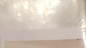 Ein Zimmer mit einer langen, dunkel gefärbten Bank an einer weißen Wand, einem an der Wand befestigten kleinen Fernseher und einem spiegel mit rotem Rahmen.