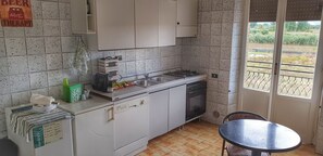 A compact kitchen with white cabinets, a dishwasher, a stove, and a sink. There's a small table and chairs in the corner. - B&B Ricci by holidayngo (Roccasecca)