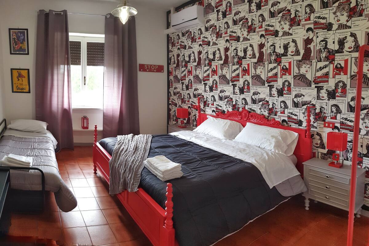 A bedroom with a bed, a nightstand, a dresser, and a window with curtains.
