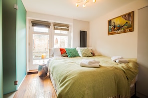 Quarto com cama, almofadas, um quadro e uma janela.