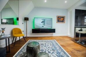 Uma sala de estar moderna com televisão de tela plana, uma poltrona amarela, um tapete estampado e piso de madeira.