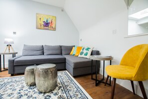 Uma sala de estar moderna com um sofá cinzento, uma poltrona amarela e um tapete estampado.