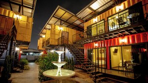 A courtyard with a fountain, outdoor seating, and a staircase leading to a balcony.