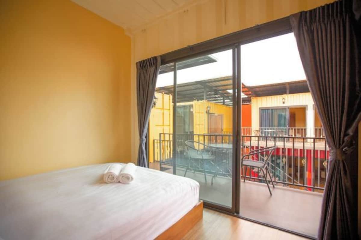 Hotellihuone, jossa on sänky, parveke, jossa on pöytä ja tuolit, sekä näkymä rakennuksen ulkopuolelle.
