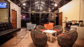 A modern indoor space with a high ceiling, glass walls, and a variety of seating options including a sofa, chairs, and a table.
