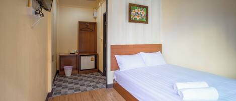 A hotel room with a bed, a wooden floor, a small desk with a trash bin, and a wall-mounted air conditioner.