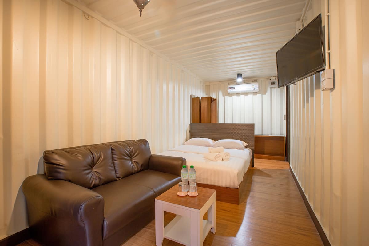 Une chambre d’hôtel avec un canapé en cuir marron, une petite table blanche sur laquelle sont posées des bouteilles, un lit avec du linge de lit blanc et un téléviseur fixé au mur.