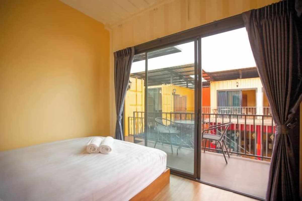 Une chambre d’hôtel avec un lit, un balcon doté d’une table et de chaises, et une vue sur la façade de l’immeuble.