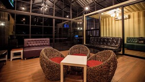 A modern interior with a high ceiling, large windows, and seating arrangements including a sofa and chairs.