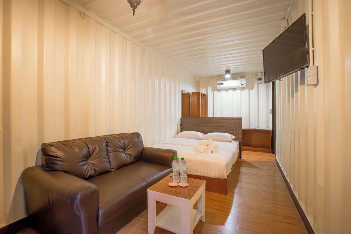 Une chambre d’hôtel avec un canapé en cuir marron, une petite table blanche sur laquelle sont posées deux bouteilles et des verres, un lit avec du linge de maison blanc et un téléviseur fixé au mur.