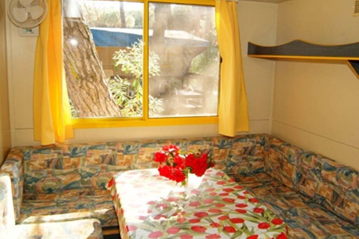 A room with a sofa bed, a window with yellow curtains, and a fan on the wall.