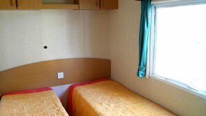 Un dormitorio de caravana pequeño con dos camas, una ventana con cortinas y armarios de madera sobre las camas.